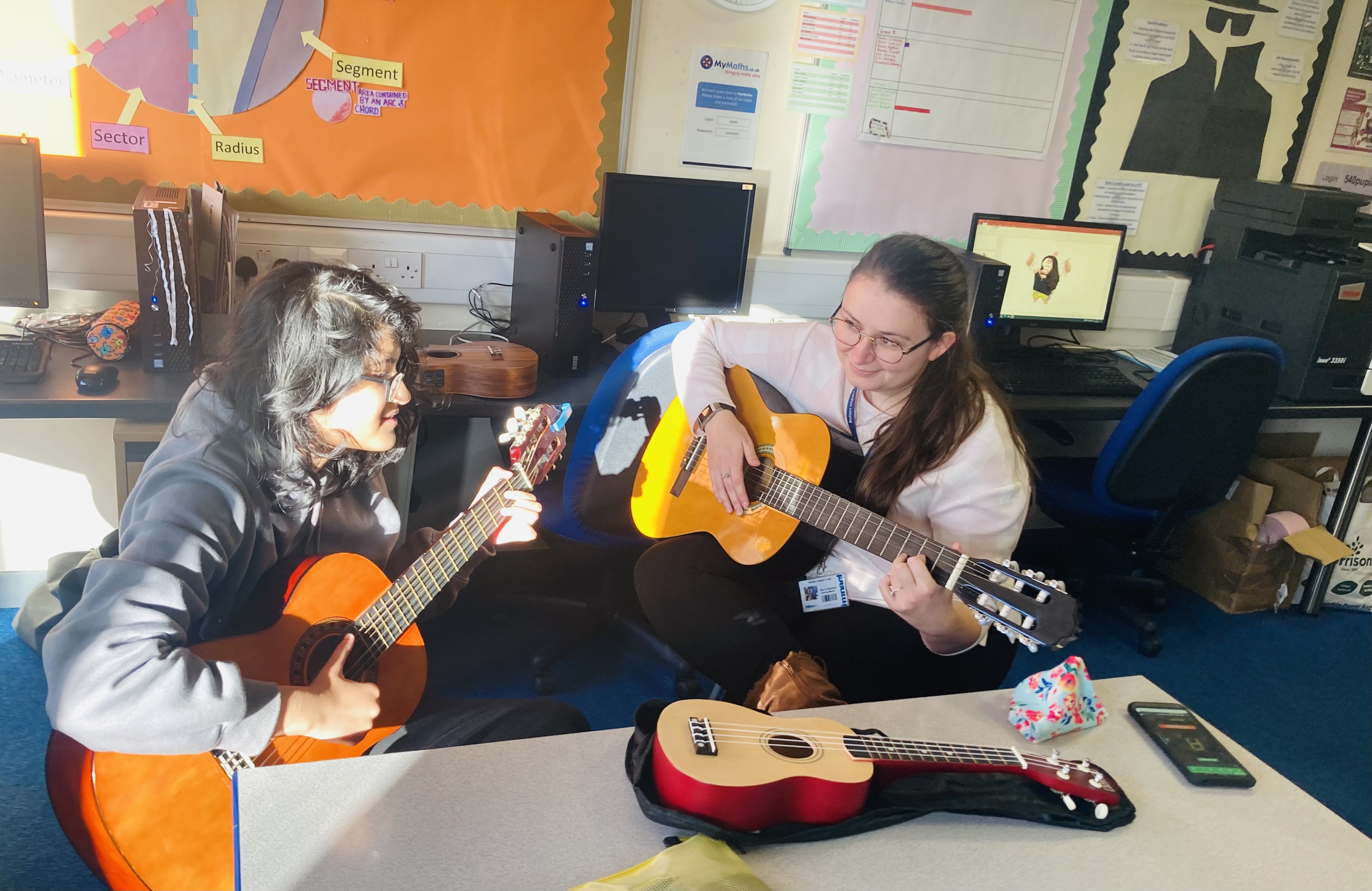 two girls play guitar in a school room