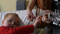 Patient on bed holding out to strum a guitar 