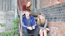 three people sitting on stairs outside of a building, a plant growing on the left
