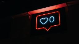 Neon light in the shape of a notification bubble, a heart shape to represent the number of likes, and the number 0 next to it.