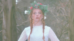 Image of Crysalice. She has red hair in two braids, is wearing a white lace dress and a floral head piece. 