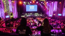 Two people on a balcony with Youth Music on their t-shirts, looking out over the Youth Music Awards event