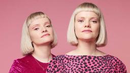 Image of Talk Like Tigers. They both have blonde bobs with short fringes and wear pink tops. They stand against a pink background.