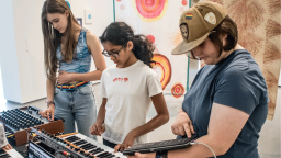 Three young women making music on keyboards, iPad, laptops and mixing desk