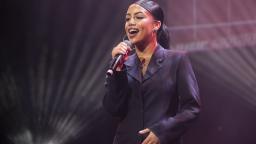 a woman sings on stage. she is wearing a black suit