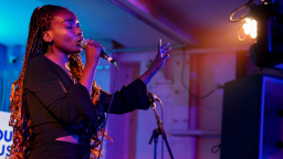 a black woman with long braids sings into a microphone on stage