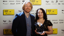 a man with strawberry blonde hair and a woman with dark brown curly hair hold an award 