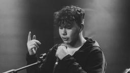 a teenage boy sings into a microphone. the photo is in black and white.