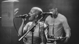 a woman with a shaved head sings into a mic