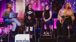 Four young women on stage talking in a panel at a NextGen Community Event