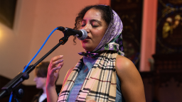 a woman wearing a silk head scarf closes her eyes and sings into a microphone