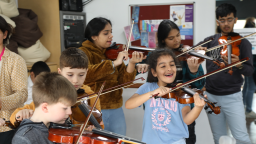 a group of children learn violin in a classroom