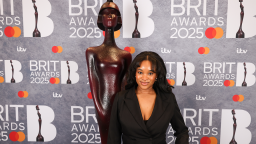 maya egbo poses in front of a branded brit awards wall and brits statue