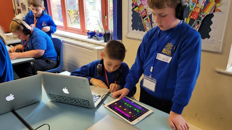 Two young boys using laptops and tablets to make music. 