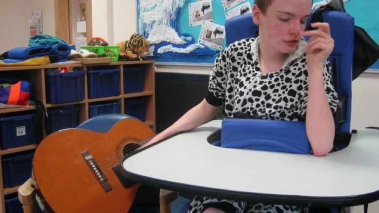 A young person sat in a chair next to a guitar