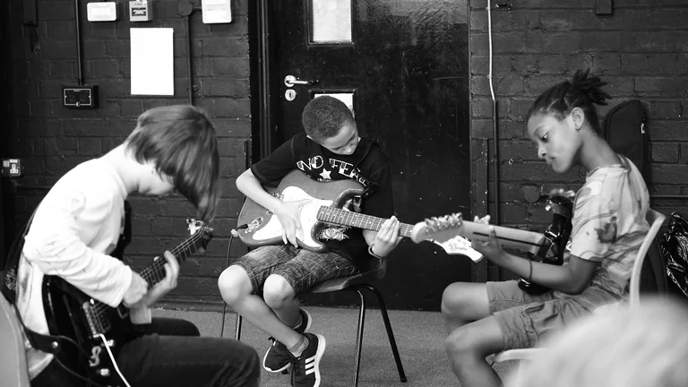 three young people playing guitar together