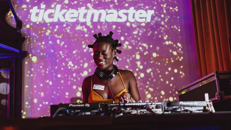 Girl smiling as she DJs on stage, with purple and glittery screen behind her