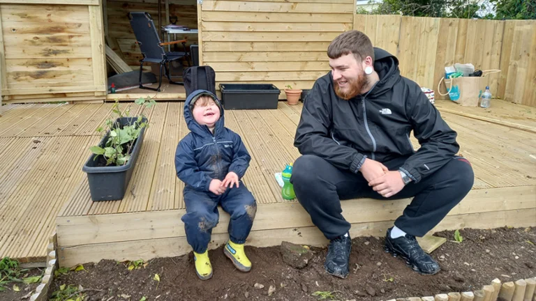 A father and son sit in a garden laughing together