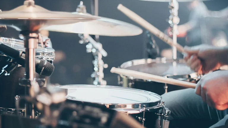 Young person playing drums for a band during a concert