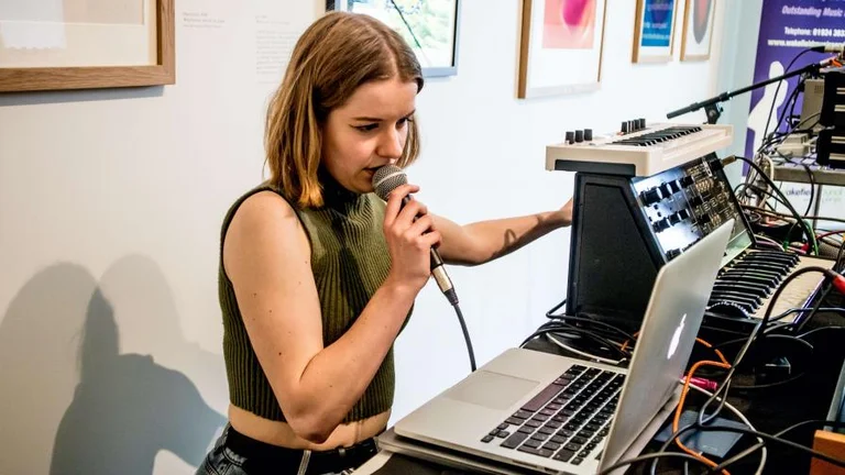 Young person with a microphone standing in front of a laptop and music production equipment