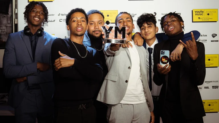 Young Group of people celebrating winning a Youth Music award and showing the prize to the camera