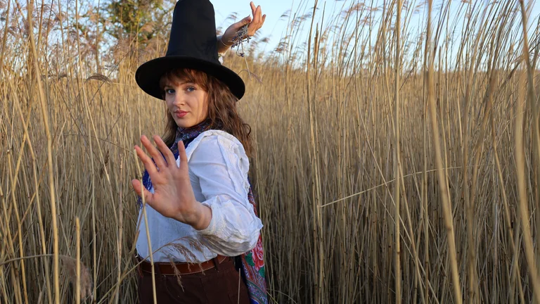 Mari Mathias dances in a wheat field in a black hat and white shirt