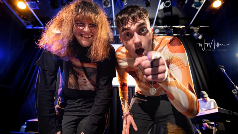 Two young people looking and pointing at the camera from a stage. 