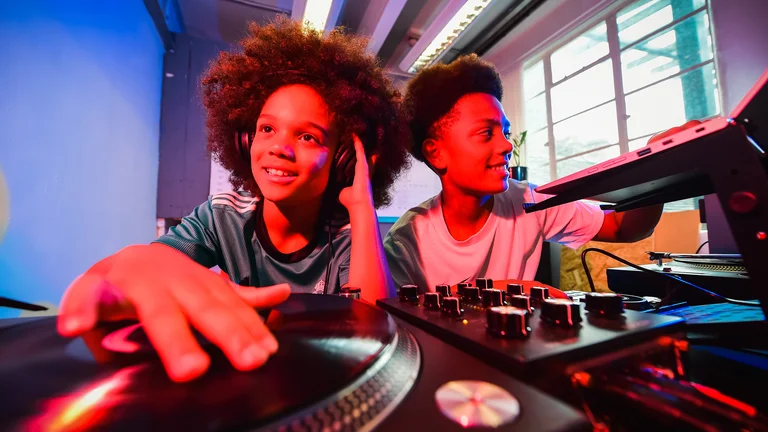 two young boys on a dj deck, faces lit up in orange