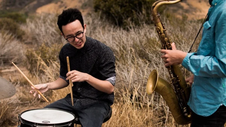 2 men, one drumming and one playing saxophone