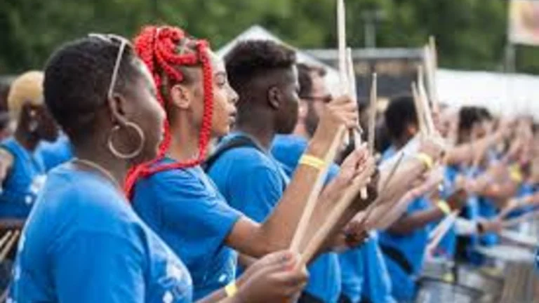 young people outside in summer drumming with drums around their necks. All wearing blue T-shirts