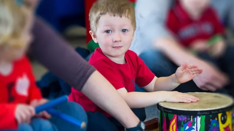 young boy playing a drum on the floor with his hands