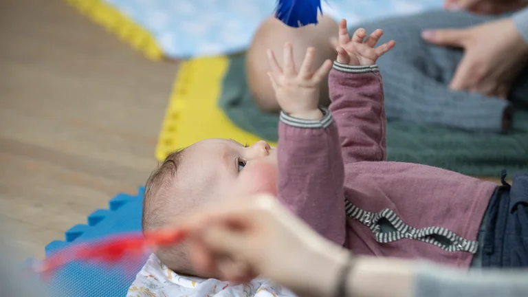 Baby lying on a mat reaching up to grab a blue feather