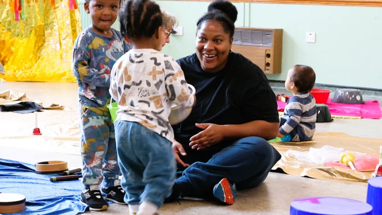 a parent and child play at a music project. two other children are seen in the background