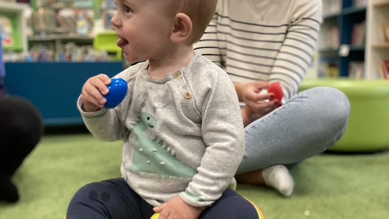 child sat on a cushion playing with egg shakers and smiling