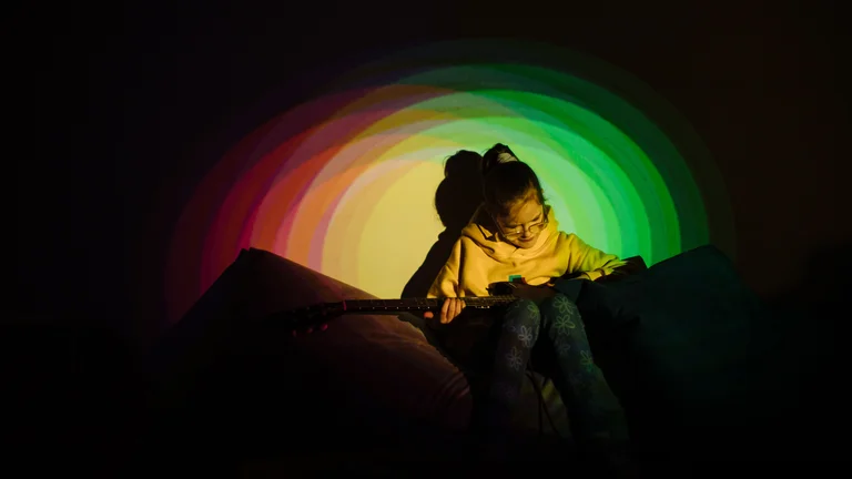 Image of young person lit by a circle of green and yellow lights interacting with multisensory equiptment.