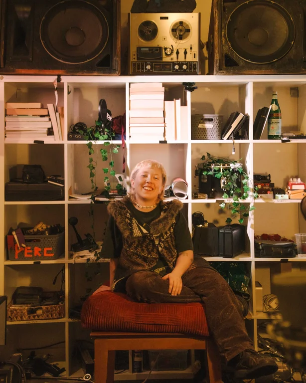 SOPH sits in front of some shelves stacked with music gear