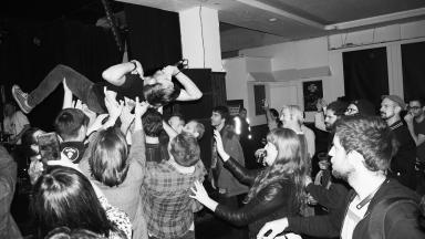 black and white photo of a live performance, where a male musician is crowd surfing