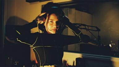person in dark room holding hands to ears over headphones 