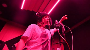 Young person with braided hair, wearing a black beanie hat and a white t-shirt, singing in a studio