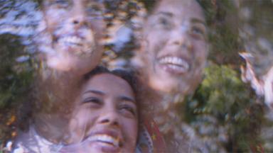 blur of three faces smiling seen through a window with reflection of trees outside
