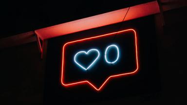 red neon sign shaped like a speech mark, with white heart and circle neon shapes inside it