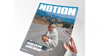photo of a hand holding Notion Magazine, a women kneeling down on a road is on thefront cover