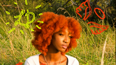 young person with a red afro sitting in a field 