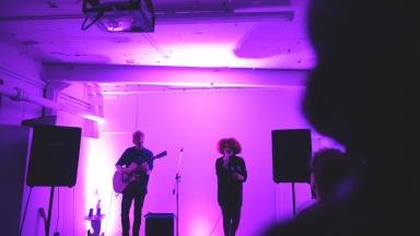 two musicians perform in a purple lit room