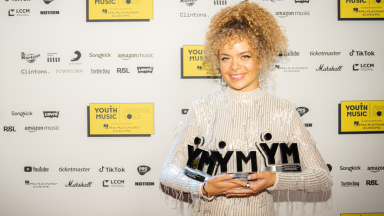 eva wears a white sequin jumpsuit and holds three youth music awards
