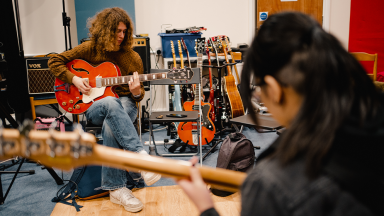 two people play electric guitars in a music room