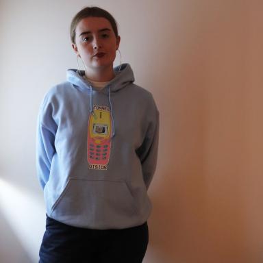 young person wearing a hoody in front of a white wall
