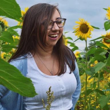 Candid photo of Zahra Baz standing in a Sunflower field, looking away from the camera and smiling.