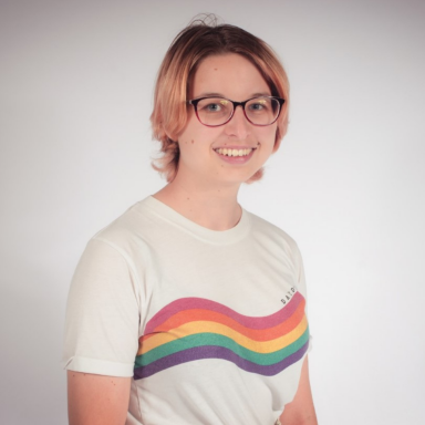 Headshot of Lydia Greatrix smiling and wearing a white t-shirt with a rainbow going across it.