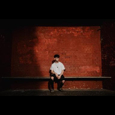 Jack wearing white t-shirt and ripped jeans, sitting in front of red brick wall